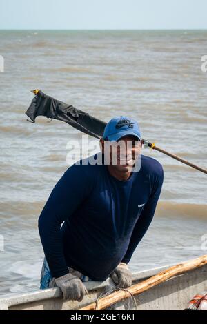 Ryohacha, La Guajira, Kolumbien - 30 2021. Mai: Lächelnder lateinischer Mann schiebt ein altes weißes Fischerboot auf der Meeresküste in Camarones Stockfoto