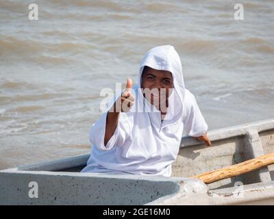 Ryohacha, La Guajira, Kolumbien - 30 2021. Mai: Junger schwarzer Latein in weißem Smiles an der Kamera, während er auf einem Boot sitzt Stockfoto