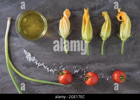 Flaches Gemüse der Saison Frische Zucchini-Blüten männliche Zucchini-Blüten Squash-Blüten mit Tomaten und grünen Zwiebeln, Olivenöl. Frische Bio-Rohprodukte. Stockfoto