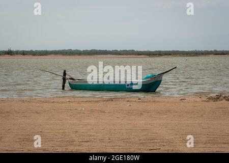 Ryohacha, La Guajira, Kolumbien - 30 2021. Mai: Kleines weißes und grünes Boot, das am Sandstrand von Camarones an einen Holzstock gebunden ist Stockfoto