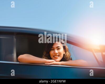 Reise der glücklichen asiatischen Frau mit kurzen Haaren mit Unschärfe-Bewegung von schwarzen Auto Bewegung auf blauem Himmel Hintergrund. Weibliche Reisende genießen und lächeln dabei Stockfoto