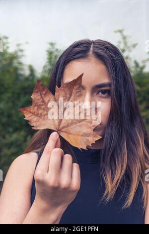 Porträt eines jungen Mädchens aus Latina, das ihr halbes Gesicht mit einem Ahornblatt bedeckt und ein Auge zeigt Stockfoto