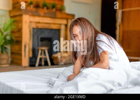 Foto von einem preteen asiatische Mädchen aufwachen. Sie sitzt mit zerzaust geschräunten Haaren auf dem Bett und will nicht aufstehen und zur Schule gehen. Der Urlaub ist vorbei. Stockfoto