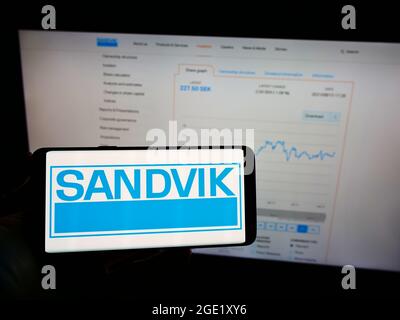 Person, die Mobiltelefon mit dem Logo des schwedischen Ingenieurunternehmens Sandvik ab auf dem Bildschirm vor der Geschäftswebseite hält. Konzentrieren Sie sich auf die Telefonanzeige. Stockfoto