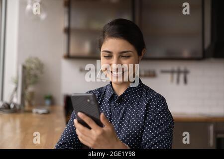 Attraktive lächelnde indische Frau schaut auf Smartphone-Bildschirm Stockfoto