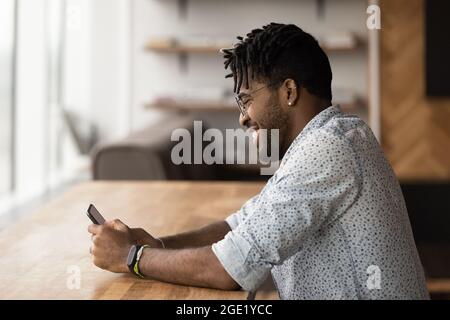 Attraktiver afrikanischer Mann sitzt am modernen Schreibtisch mit Smartphone Stockfoto