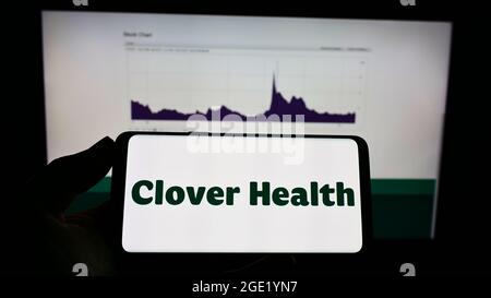 Person mit Mobiltelefon und Logo des Gesundheitsunternehmens Clover Health Investments Corp. Auf dem Bildschirm vor der Webseite. Konzentrieren Sie sich auf die Telefonanzeige. Stockfoto