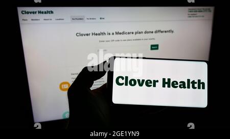 Person, die das Smartphone mit dem Logo des Gesundheitsunternehmens Clover Health Investments Corp. Auf dem Bildschirm vor der Website hält. Konzentrieren Sie sich auf die Telefonanzeige. Stockfoto