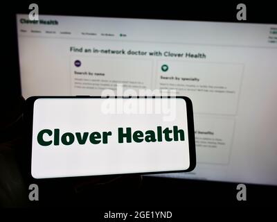 Person, die Mobiltelefon mit dem Logo des Gesundheitsunternehmens Clover Health Investments Corp. Auf dem Bildschirm vor der Webseite hält. Konzentrieren Sie sich auf die Telefonanzeige. Stockfoto