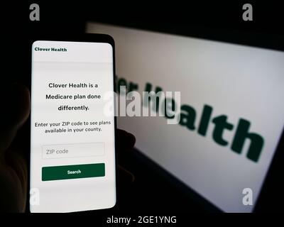 Person mit Mobiltelefon und Webseite des Gesundheitsunternehmens Clover Health Investments Corp. Auf dem Bildschirm mit Logo. Konzentrieren Sie sich auf die Mitte des Telefondisplays. Stockfoto