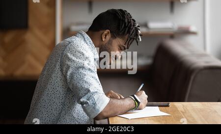 Afrikanischer Kerl sitzt am Tisch und füllt den Fragebogen aus Stockfoto