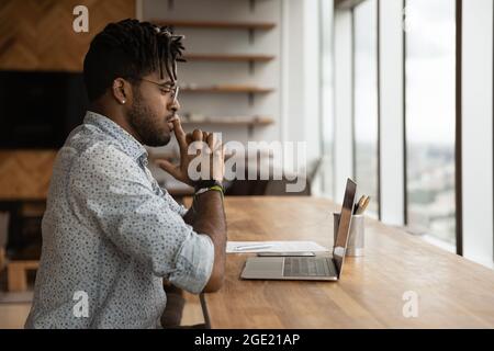 Nachdenklicher afrikanischer Mann schaut auf Laptop-Bildschirm denkt über Aufgabe Stockfoto