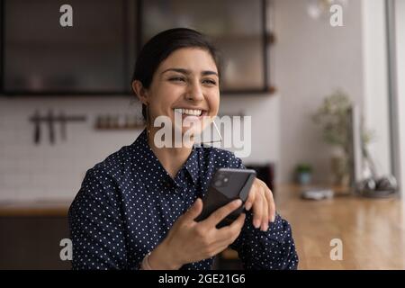 Indische Frau sitzen drinnen halten Smartphone lachend Stockfoto