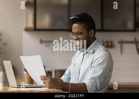 Glücklicher afrikanischer Kerl, der gute Nachrichten in einem Brief liest Stockfoto
