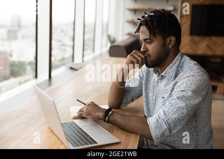 Afrikanischer Kerl sitzt am Tisch betrachtet Laptop betrachten Aufgabe Stockfoto