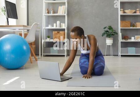 Glückliche junge afroamerikanische Frau schaltet Sporttraining Video-Lektion auf Laptop. Stockfoto