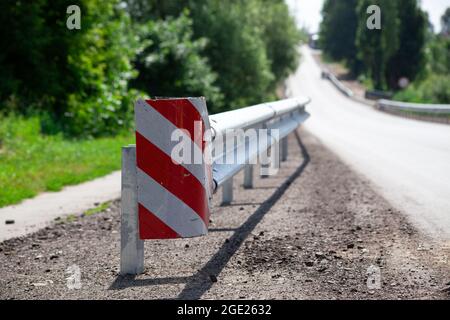 Rote Straßenreflektoren entlang der Straße. Metalleinzäunung von Barriere-Typ, Nahaufnahme. Straßen- und Verkehrssicherheit. Reflektierende Farbe auf dem Schild. Mittlere Barriere Stockfoto