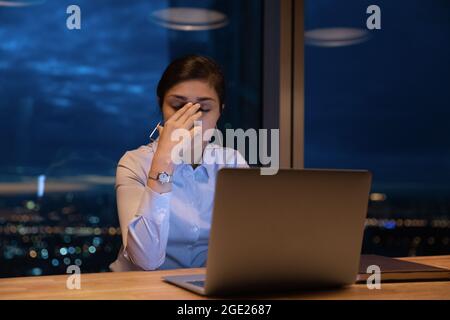 Müde indische Büroangestellte arbeiten spät mit einem Laptop im Büro Stockfoto