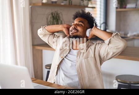 Junger Student mit Laptop und Kopfhörern zuhause, reating nach dem Studium. Stockfoto
