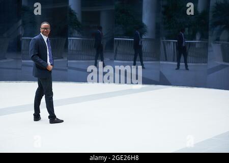Ein gutaussehender, lächelnder junger Geschäftsmann, der vor dem Bürogebäude steht, sich umkehrt und die Kamera anschaut Stockfoto