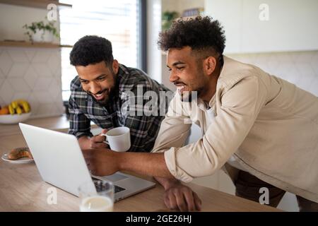 Junge Studentenbrüder, die zuhause in der Küche mit einem Laptop arbeiten. Stockfoto