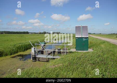 Sehr kleines niederländisches Wehr (niederländisch: Ventilwehr) mit Sonnenkollektoren in der Nähe eines Grabens. Das Wehr regelt die Wasserabflusskapazität des Oberflächenwassers. Stockfoto