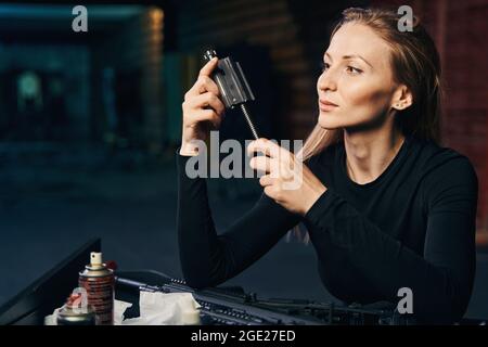 Fokussierte Militärfrau, die einen Waffenteil in ihren Händen inspiziert Stockfoto