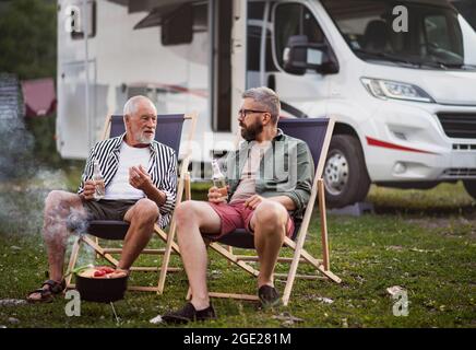 Reifer Mann mit Seniorvater im Freien auf dem Campingplatz reden, Grillen auf Caravan-Urlaubsreise. Stockfoto