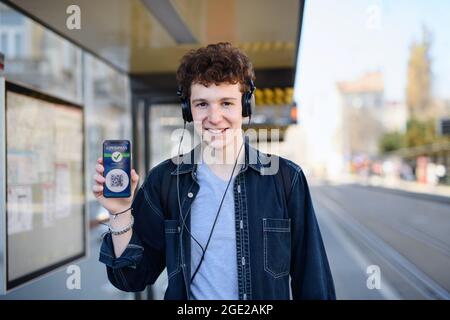 Porträt eines jungen Mannes, der im Freien in der Stadt steht, zeigt covid Pass auf dem Smartphone. Stockfoto