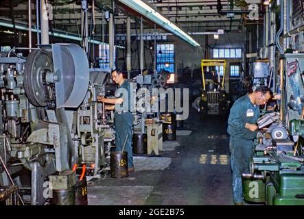 Die Betriebsdauer der Fabrik wurde 1959 bei der Positive Lock Company, Washington DC, USA, beobachtet. Die Arbeiter sind in dieser Werkstatt an Drehmaschinen, großen Bohrern und Schleifwerkzeugen. Im Hintergrund ist ein kleiner Gabelstapler zu sehen. Kleine Fabriken, in denen Waren mit qualifizierten lokalen Arbeitskräften hergestellt wurden, waren in den Jahren vor der Automatisierung und der preiswerteren Konkurrenz im Ausland sehr üblich in Amerika. Dieses Bild stammt aus einer alten amerikanischen Kodak Amateur-Farbtransparenz – einem Vintage-Foto aus den 1950er Jahren. Stockfoto