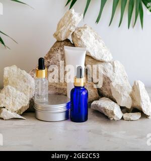 Set natürliche Schönheit kosmetische Hautpflegeprodukte mit Palmblatt-Pflanze auf Stein Sockel, Steinhaufen balancierende Steine grauen Hintergrund. Serumcrembutter Stockfoto