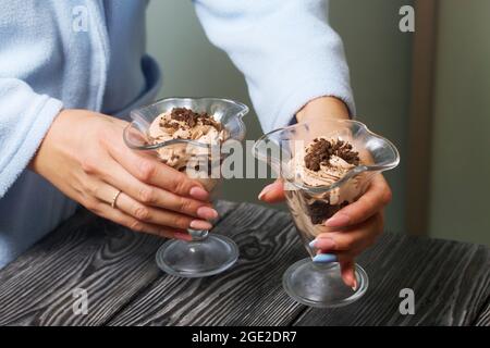 Eine Frau stellt einen Nachtisch aus Creme und Keksbröseln auf den Tisch. Nahaufnahme. Stockfoto