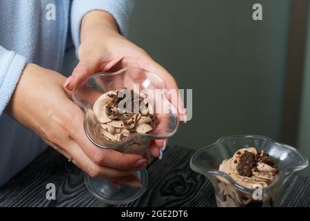 Eine Frau stellt einen Nachtisch aus Creme und Keksbröseln auf den Tisch. Nahaufnahme. Stockfoto