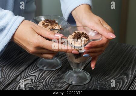 Eine Frau stellt einen Nachtisch aus Creme und Keksbröseln auf den Tisch. Nahaufnahme. Stockfoto