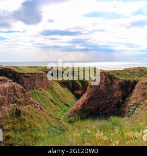 Grünes Gras, Rasenflächen an den Hängen der Berge in der Nähe des Meeres gegen den blauen Himmel gewachsen. Hügel der Berge und Hänge des Kaps sind mit halb Gras und überwuchert Stockfoto