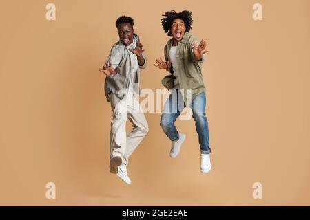 Zwei Fröhliche, Emotionale Afroamerikanische Jungs Springen Über Beigen Studiohintergrund Stockfoto