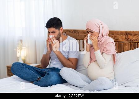 Das junge, schwanger-muslimische Paar bekam eine Grippe, hatte eine laufende Nase, saß zu Hause auf dem Bett und niesen in Papiergewebe Stockfoto