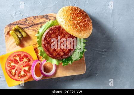 Hamburger Zutaten, aufgenommen von oben auf blauem Hintergrund mit einem Platz für Text. Sesambrot, Fleischpastete, grüner Salat und rote Zwiebeln, Schuss über den Kopf Stockfoto