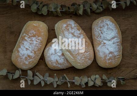 Drei hausgemachte süße Creme weiche Brötchen und bestreut mit Puderzucker auf alten rustikalen Holztisch. Bäckerei- und Dessertkonzept, selektiver Fokus. Stockfoto