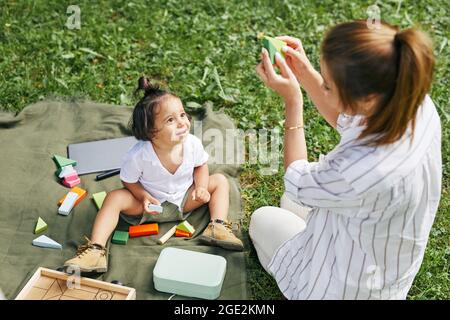 Hochwinkel-Porträt von niedlichen kleinen Jungen mit jungen Mutter im Park spielen mit Spielzeug genießen Sommer im Freien Stockfoto