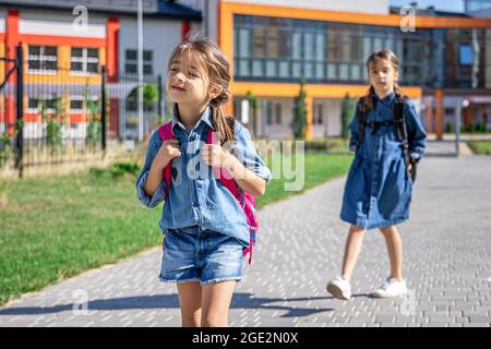 Schüler der Grundschule. Mädchen mit Rucksäcken in der Nähe der Schule im Freien. Beginn des Unterrichts. Erster Herbsttag. Stockfoto