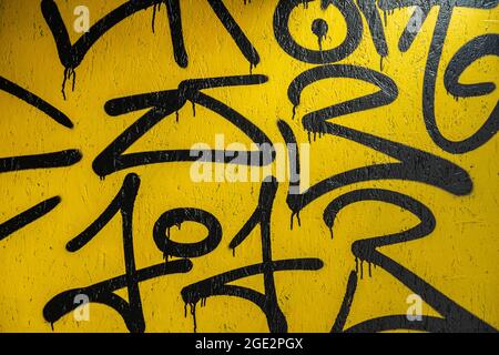 Abstraktes Fragment kreativer schwarzer Kritzeleien auf gelb lackierter Betonwand. Aerosoldesign. Moderner Hintergrund Stockfoto
