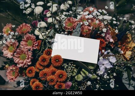 Moody feminine Hochzeit, Geburtstag Mockup Szene. Nahaufnahme einer leeren Papierkarte, Geschenketikett auf buntem Blumenstrauß im Sonnenlicht. Gypsophila und Stockfoto