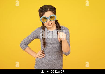 Sonnenbrillen sind gesundheitliche Notwendigkeit. Unzufrieden Kind gelben Hintergrund. Get Party started. Kid Zeigefinger. Porträt des Mädchens in lustigen Brillen. Jung Stockfoto