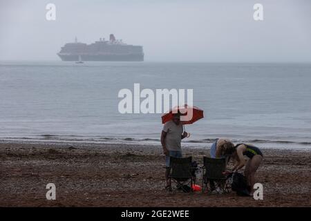 Urlauber trotzen den Elementen am Goodrington North Beach in Paignton, Devon, der von Gewitterschauern getroffen wurde und einige Touristen dazu zwingt, für Deckung zu laufen, Großbritannien. Stockfoto