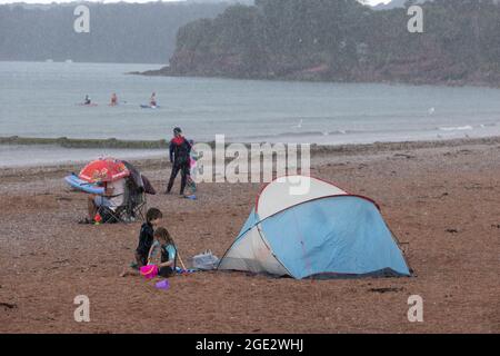 Urlauber trotzen den Elementen am Goodrington North Beach in Paignton, Devon, der von Gewitterschauern getroffen wurde und einige Touristen dazu zwingt, für Deckung zu laufen, Großbritannien. Stockfoto