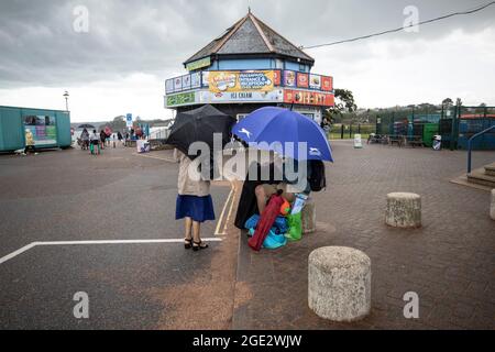 Urlauber trotzen den Elementen am Goodrington North Beach in Paignton, Devon, der von Gewitterschauern getroffen wurde und einige Touristen dazu zwingt, für Deckung zu laufen, Großbritannien. Stockfoto