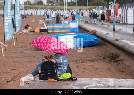 Urlauber trotzen den Elementen am Goodrington North Beach in Paignton, Devon, der von Gewitterschauern getroffen wurde und einige Touristen dazu zwingt, für Deckung zu laufen, Großbritannien. Stockfoto