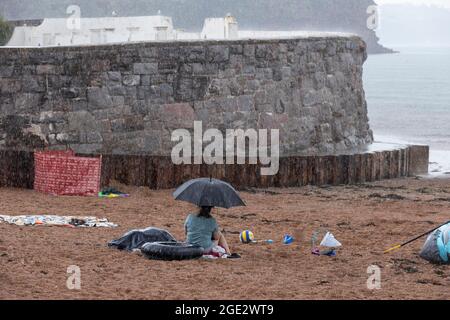 Urlauber trotzen den Elementen am Goodrington North Beach in Paignton, Devon, der von Gewitterschauern getroffen wurde und einige Touristen dazu zwingt, für Deckung zu laufen, Großbritannien. Stockfoto