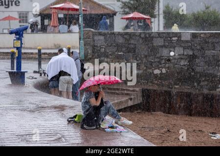 Urlauber trotzen den Elementen am Goodrington North Beach in Paignton, Devon, der von Gewitterschauern getroffen wurde und einige Touristen dazu zwingt, für Deckung zu laufen, Großbritannien. Stockfoto